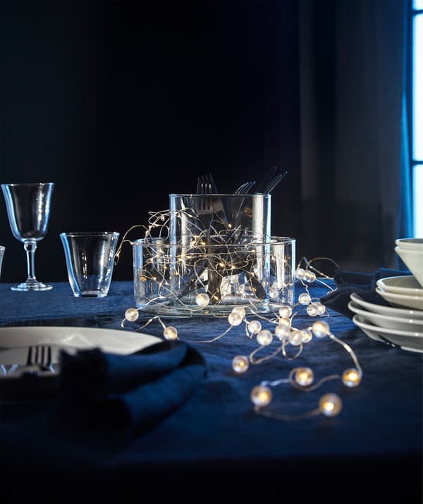 A couple of IKEA SNÖYRA LED lighting chains lying across a table amongst glasses, vases and plates.