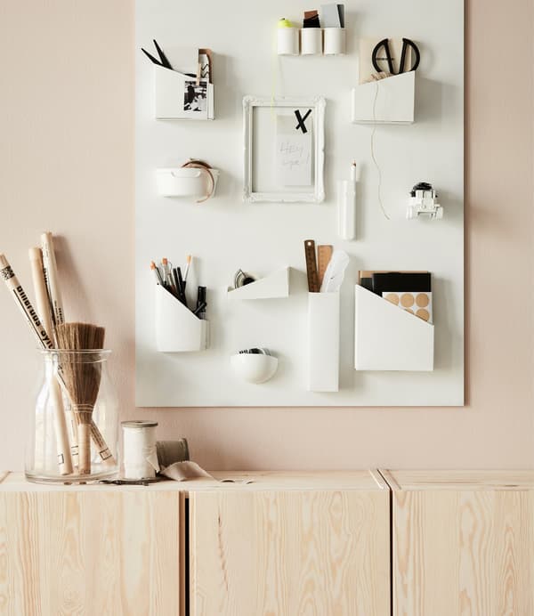A couple of IVAR cabinets in untreated wood under a wall decorated with art equipment.
