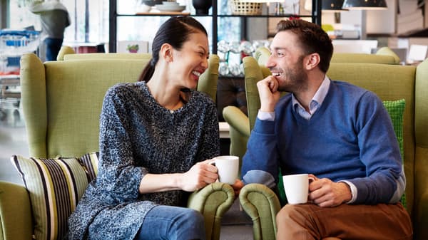 A couple sitting on comfy chair drinking coffee and laughing