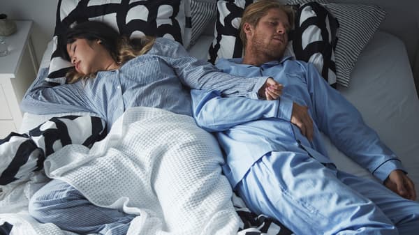 A couple sprawl across a double bed with black and white SKUGGBRÄCKA bed linen and a VÅRELD bedspread, deep in sleep.