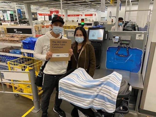 A couple with a baby carriage holding their IKEA Coffee Table Catalogue 