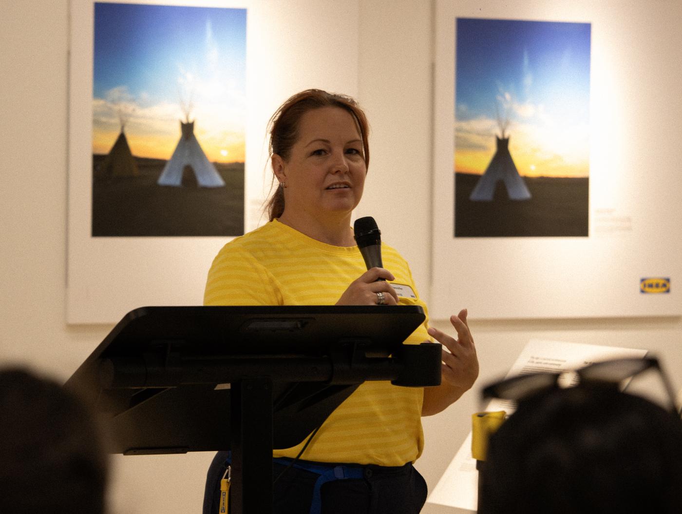 A coworker is holding a microphone and speaking at a podium.