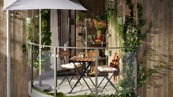 A cozy balcony with plenty of wooden tones, hanging plants, a TÄRNÖ table, TÄRNÖ chairs and a RUNMARÖ shelving unit.