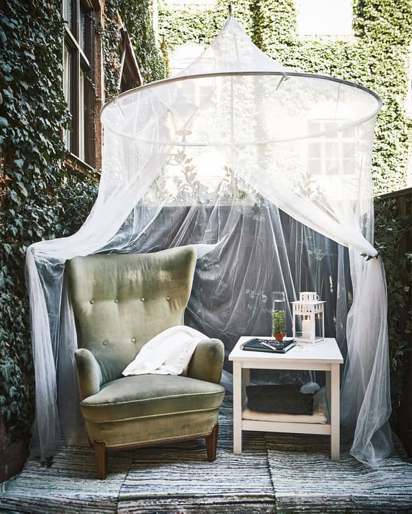 A cozy corner is set up in a corner with an armchair, a side table and a canopy hanging above.