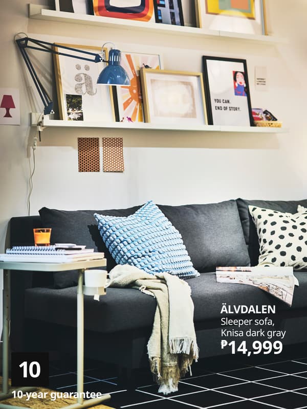A cozy dark gray sleeper sofa with colorful pillows, a table with a mug, and vibrant wall art in a stylish living room setting.