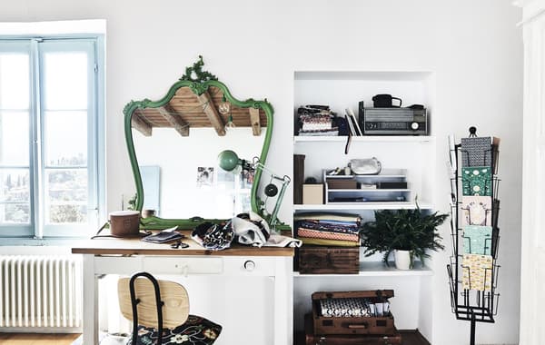 A craft space with desk, white walls and green mirror.