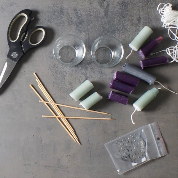 A creative collection of craft supplies, including candles, wicks, glass holders, and scissors, is displayed as if it were a DIY candle project using IKEA supplies.
