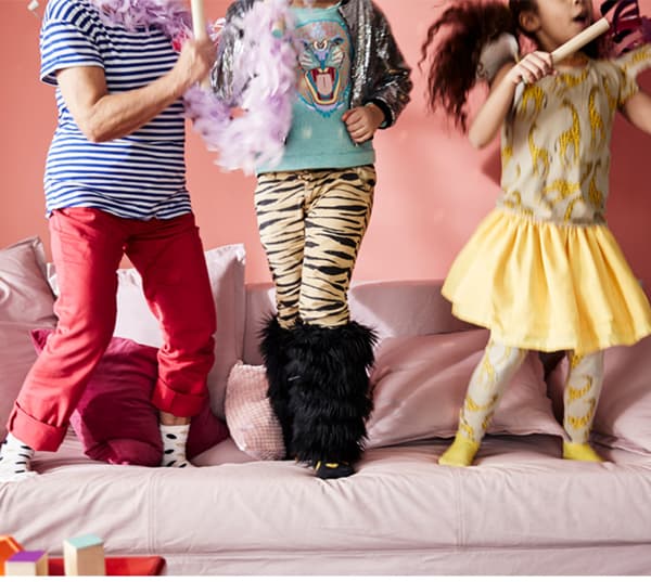 A cropped image showing three young children's legs on top of a pink sofa as they play together.