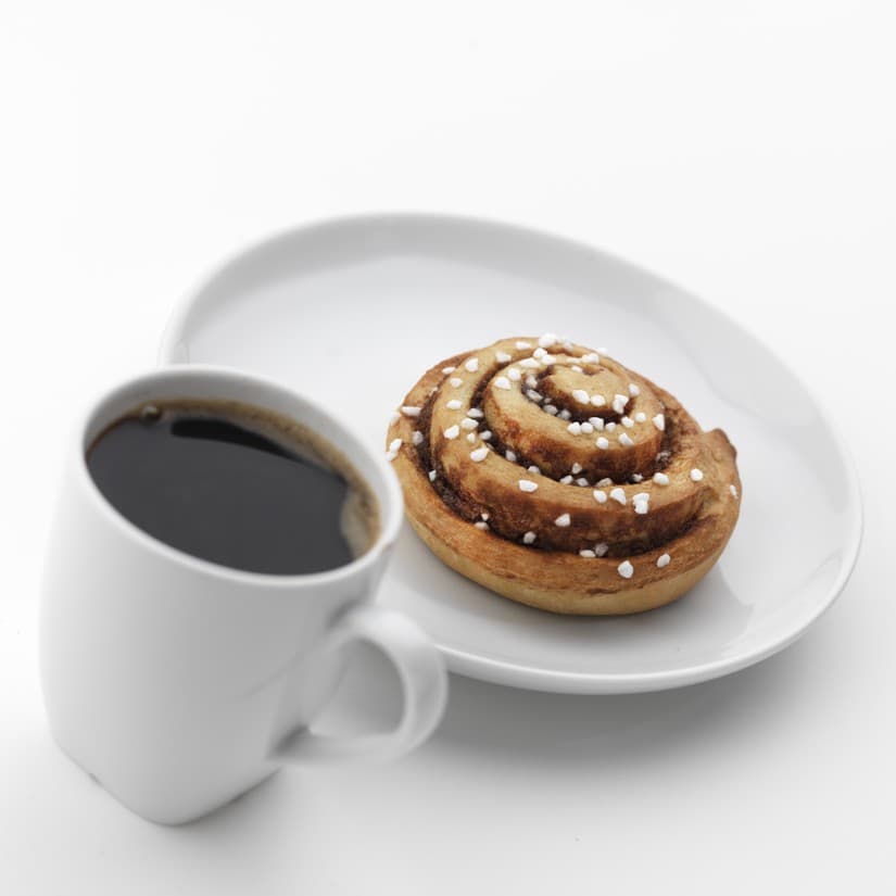 A cup of coffee next to a plate with a mini cinnamon roll