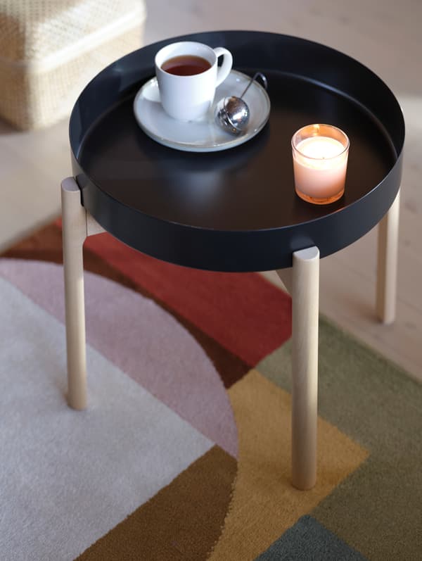 A cup of tea and strainer sit beside a lit candle, on an YPPERLIG side table.