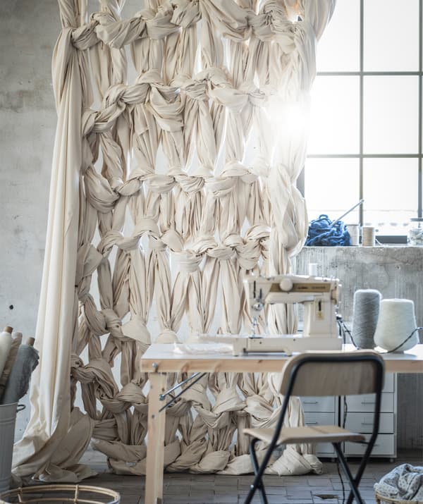 A curtain made of knotted fabric hangs behind a table with a sewing machine on top.