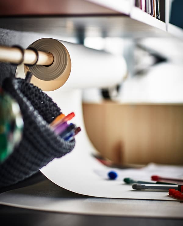 A curtain rod mounted on the wall above the desk to hold a roll of drawing paper.