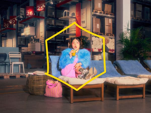 A customer sits in the IKEA warehouse on a sun lounger sipping a drink. There is a yellow fallen key overlay on the image. 