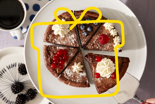 A cut up chocolate cake on a white plate, with berries and cream.