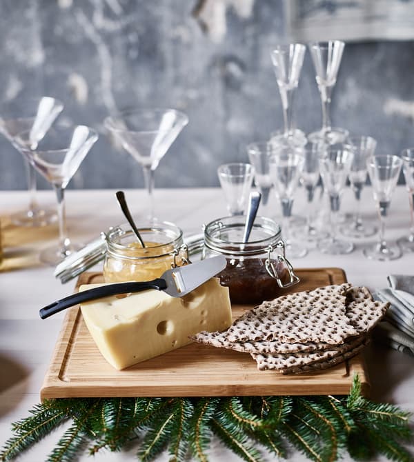 A cutting board with a block of cheese, crisp bread and jars of jam.