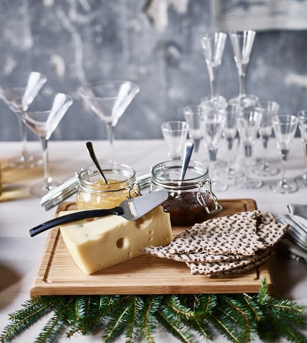 A cutting board with a block of cheese, crisp bread and jars of jam.