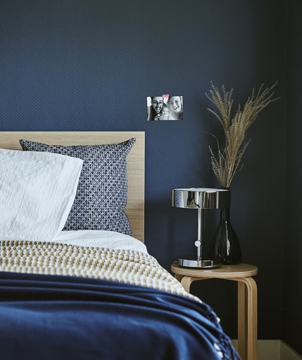 A dark blue bedroom with a bed and bedside stool.