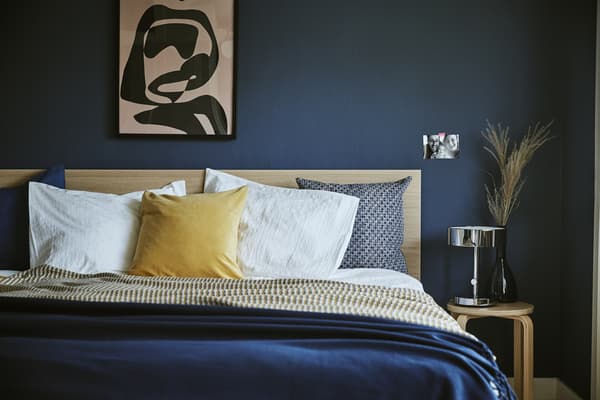 A dark blue bedroom with a bed and bedside stool.