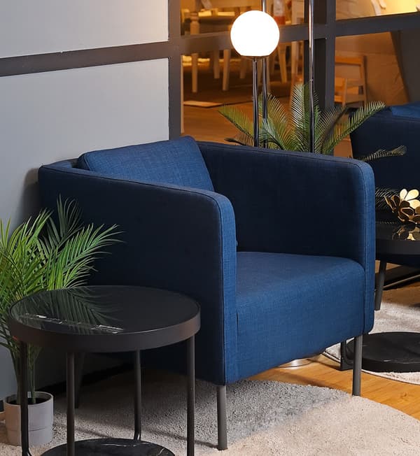 A dark blue chair with a side table and artificial plants.