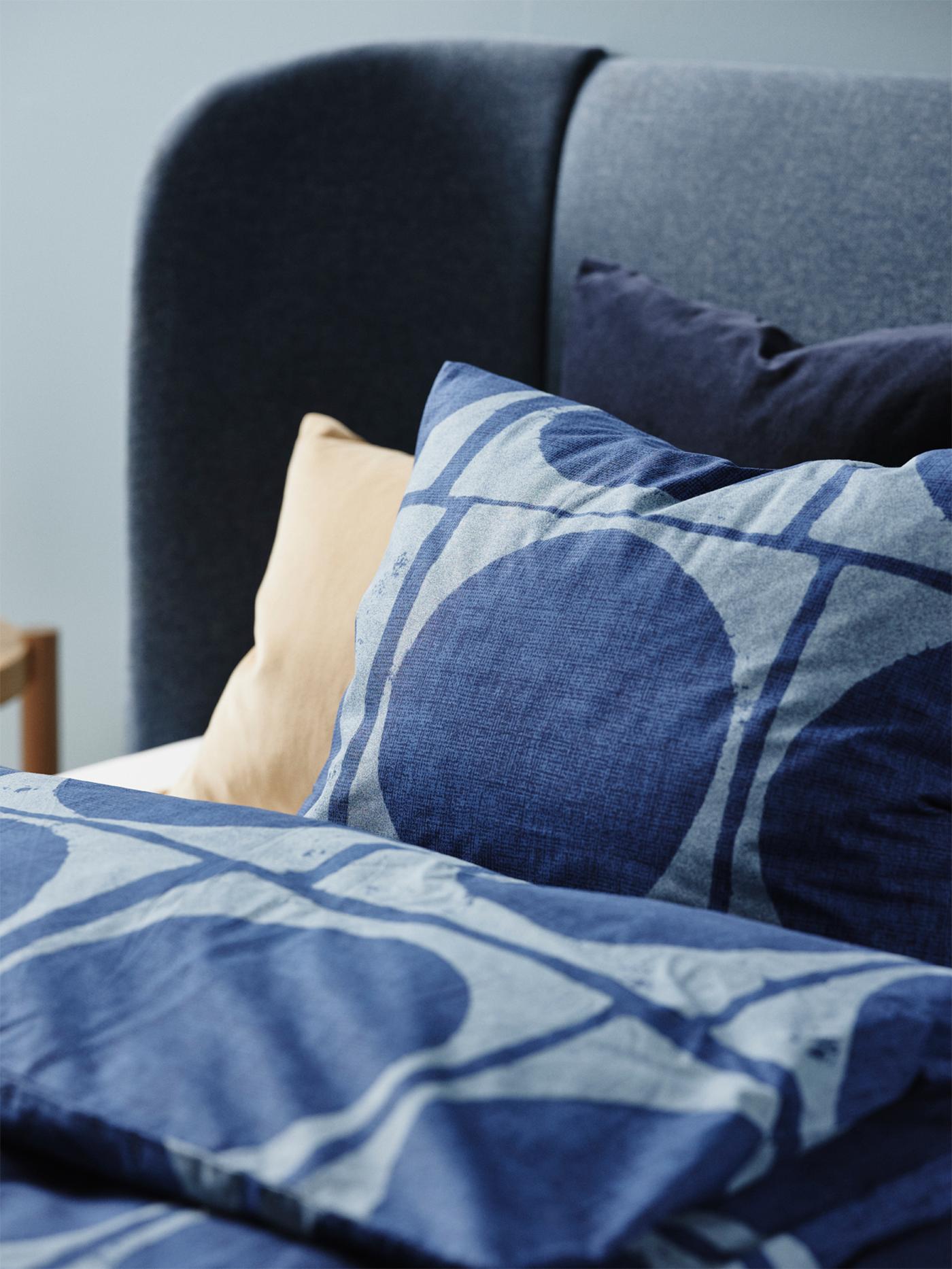 A dark blue JORDRANUNKEL pillowcase and duvet cover are on a bed. Beige and blue pillows are propped behind the main pillow.
