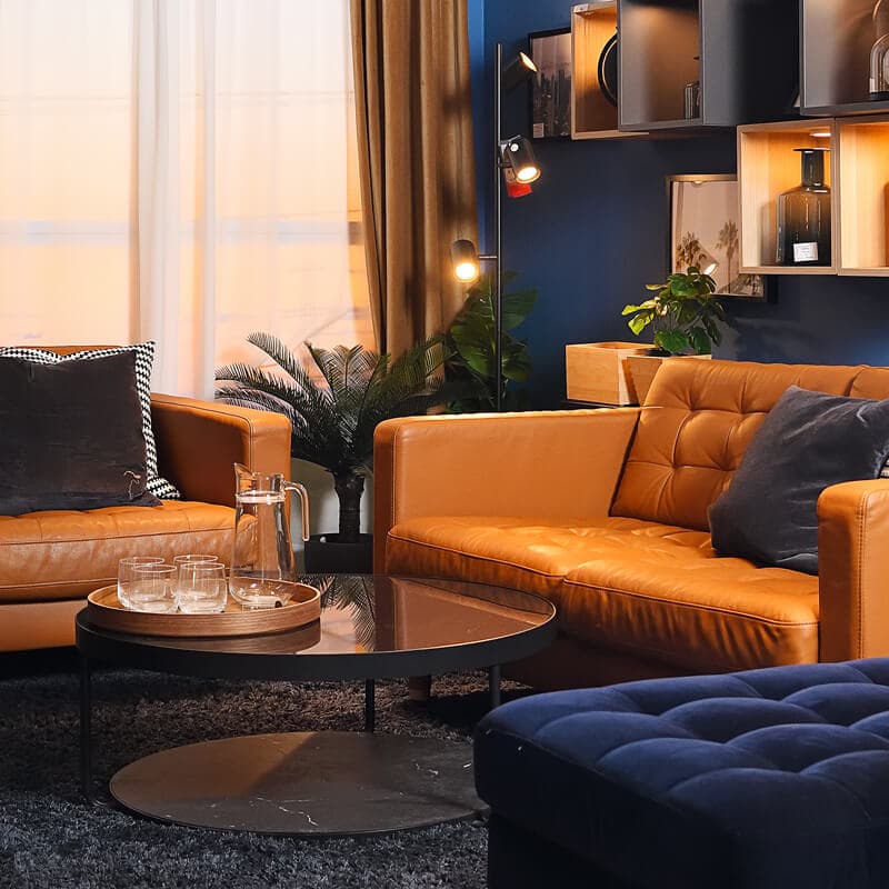 A dark blue room featuring three leather sofas and a black coffee table with a glass jug and glasses on a wooden tray.