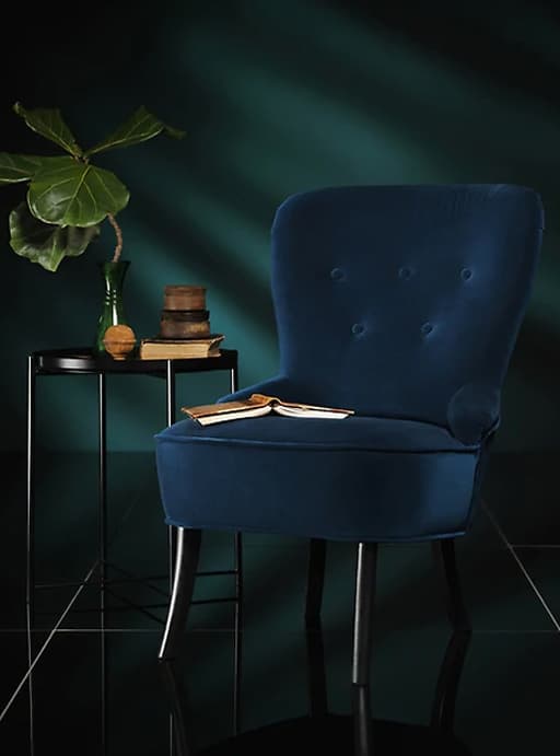 A dark blue velvet armchair next to a side table in a dark room.