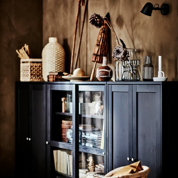 A dark brown glass-door cabinet with lots of books and decorative items in natural colours and materials.
