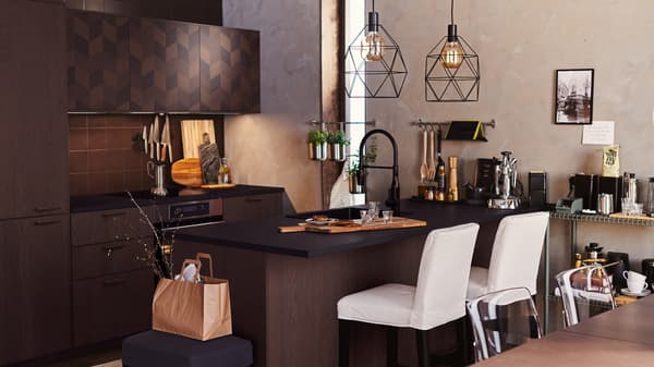 A dark brown HASSLARP/SINARP kitchen with island. White bar stools are at the island and two BRUNSTA lamps hang overhead.