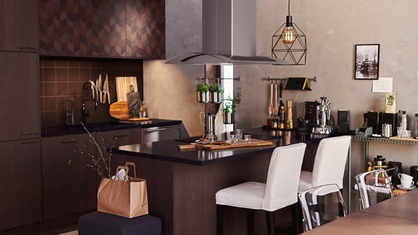 A dark brown HASSLARP/SINARP kitchen with island. White bar stools are at the island and a BRUNSTA lamp hangs overhead.