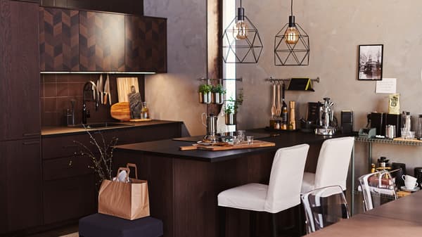 A dark brown HASSLARP/SINARP kitchen with island. White bar stools are at the island and two BRUNSTA lamps hang overhead.