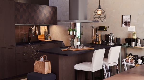 A dark brown HASSLARP/SINARP kitchen with island. White bar stools are at the island and two BRUNSTA lamps hang overhead.