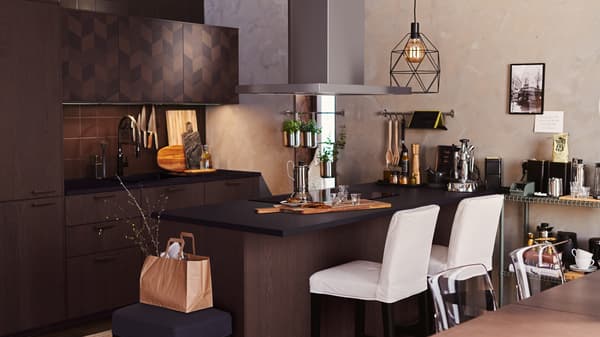 A dark brown kitchen with METOD cabinets and an island. White bar stools at the island, and a BRUNSTA lamp overhead.