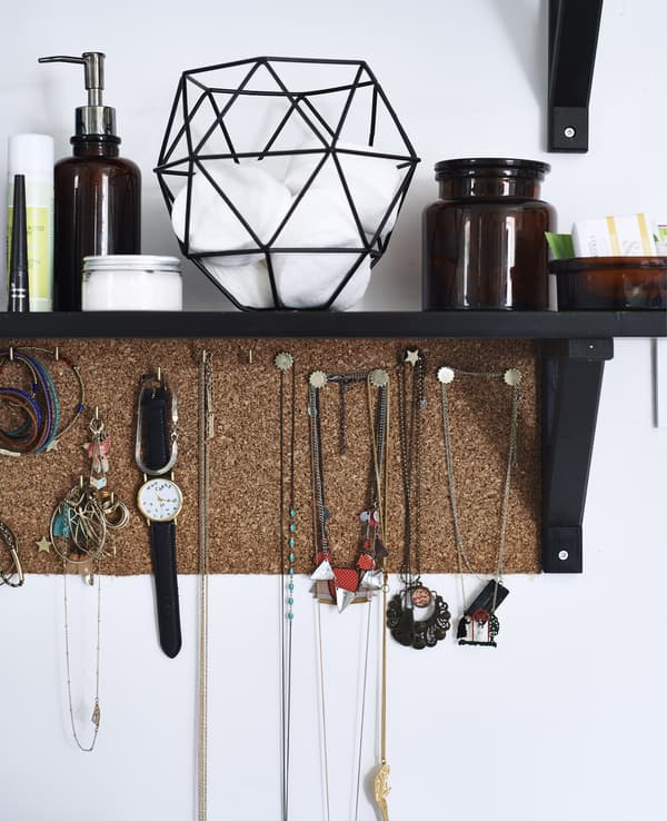 A dark brown, wall-mounted shelf and cork board filled with storage jars and jewellery.