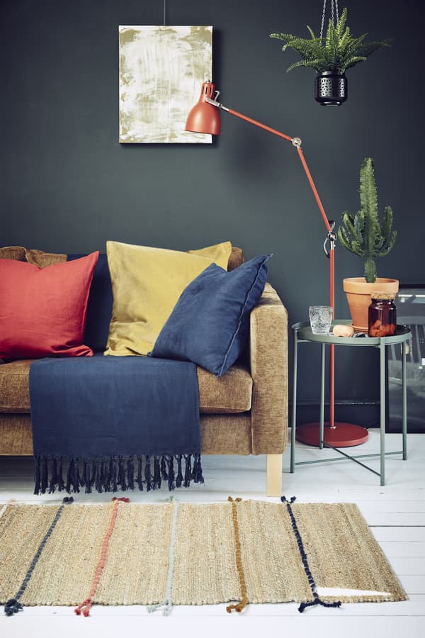 A dark-coloured living room with a sofa, lighting and bold textiles.