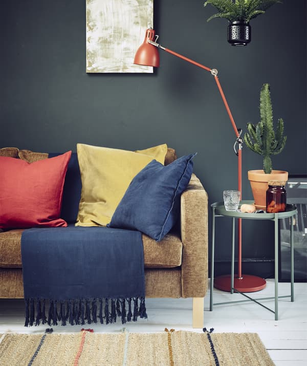 A dark-coloured living room with a sofa, lighting and bold textiles.