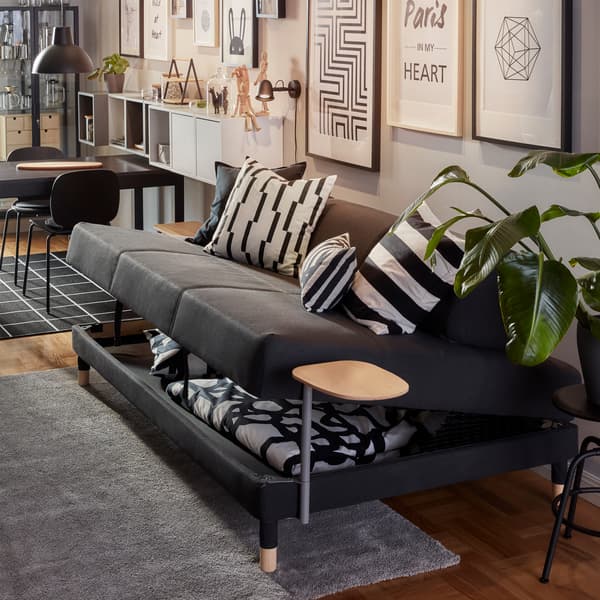 A dark gray FLOTTEBO sofa-bed where the seat has been lifted, underneath it is storage space with a duvet and a pillow.