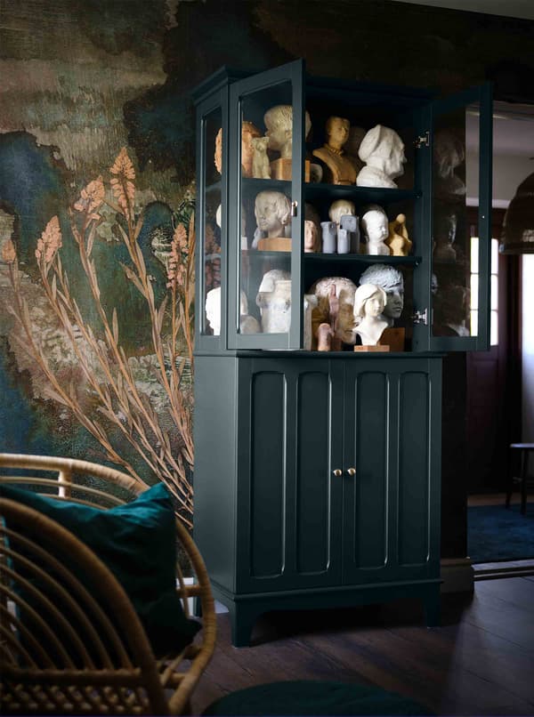 A dark green cabinet with glass doors is full of old-fashioned sculptures.