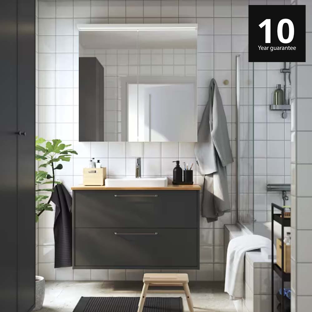 A dark grey/bamboo HAVBÄCK wash-stnd w drawers/wash-basin/tap in a bathroom setting. 10-year guarantee logo on top right corner.