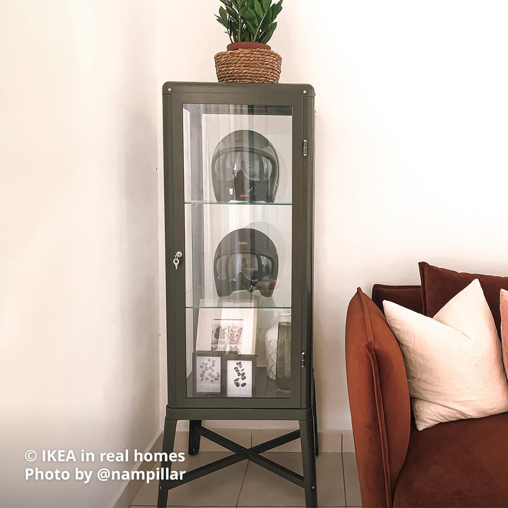 A dark grey FABRIKÖR glass-door cabinet with instagrammer's bike helmet and photo frames displayed on each shelving. Photo by instagrammer @nampillar for IKEA in real homes ©