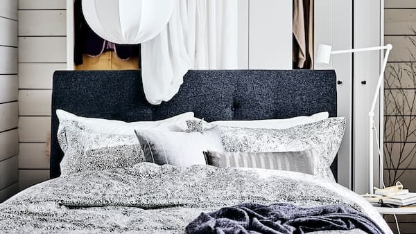 A dark grey IDANÄS upholstered bed with a white curtain and a white wardrobe behind it and a white pendant lamp above it.