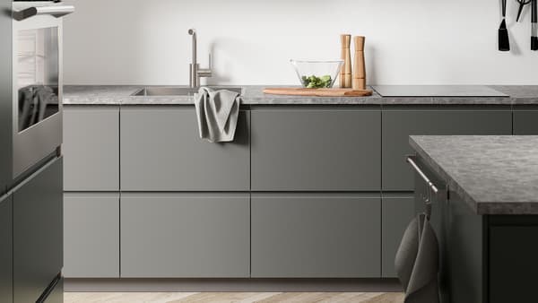 A dark grey kitchen with dark grey VOXTORP kitchen fronts, a dark grey stone-effect worktop and an island.