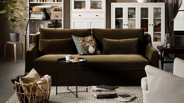 A dark olive-green 2-seat sofa, a white high cabinet with glass doors and 1 drawer, a white bookcase, a birch stool.