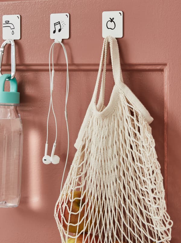 A dark-pink door fitted with graphic-motif hooks holding a water bottle, earphones and a KUNGSFORS net bag with fruit.