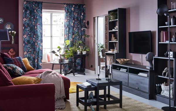 A dark red 4-seater sofa and dark brown tv bench in a living room with pink walls and floral textiles.