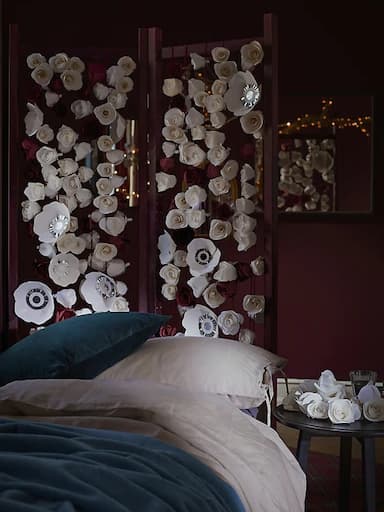 A dark red bedroom with a bed dressed in blue and white bedding and a floral screen.