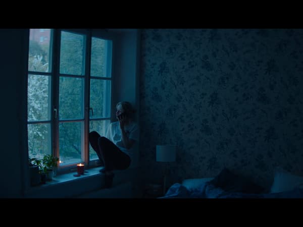 A dark room with a person sitting on a windowsill looking outside.