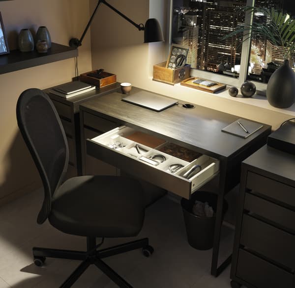 A dark workspace area with a black desk and desk chair, lit with a black work lamp.