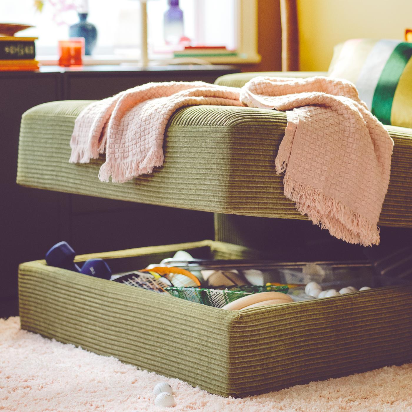 A dark yellow-green JÄTTEBO chaise longue has a hidden storage compartment opened, showing things inside.