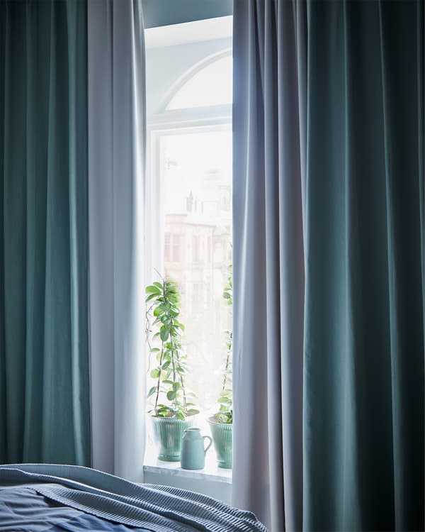 A daylight scene in a bedroom window that's surrounded by light grey and green curtains.