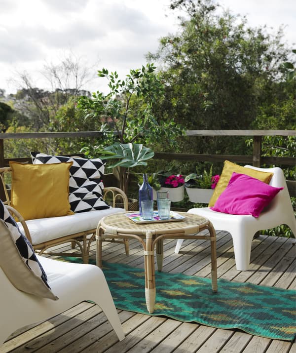 A deck area with rattan sofa and table, plastic armchairs, a colourful rug and cushions.